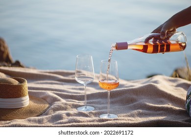 Woman hand pouring rose wine from bottle into glasses on the beach. - Powered by Shutterstock