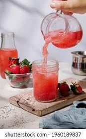 Woman hand pouring strawberry juice, coconut water, nata de coco, chia seeds in a glass.
