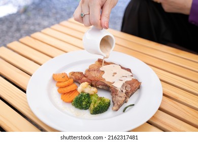 Woman Hand Pouring T-bone Steak Sauce On The Plate