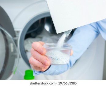 Woman hand pouring washing powder. Measuring cup with granular solid detergent. Open washing machine.