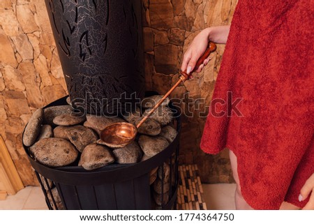 Woman hand pouring water into hot stone in the wooden traditional sauna spa room.
