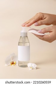 A woman hand pumping liquid on a make-up remover pad from a cosmetic bottle near orchid flowers on beige close up, label mockup. Skincare beauty product package, minimal composition - Shutterstock ID 2210260559