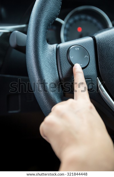 A woman hand pushes the volume control button on a\
steering wheel.