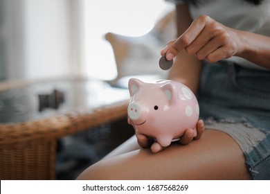 Woman hand putting coin into pink piggy bank, Finance or Savings concept.
