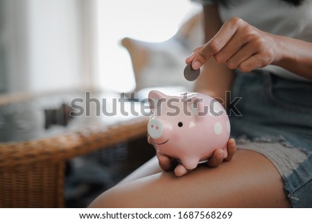 Woman hand putting coin into pink piggy bank, Finance or Savings concept.