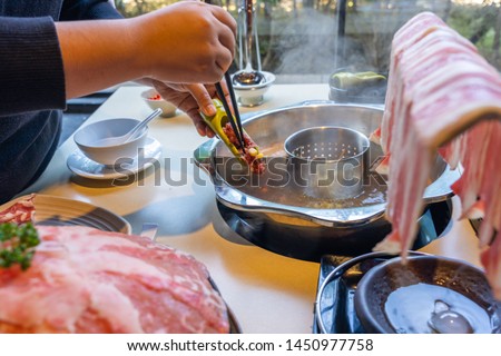 Woman hand putting meat ball into the hotpot