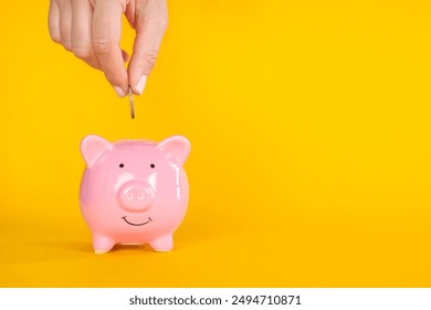 Woman' hand putting money into pink piggy bank on yellow background. Saving money with cute piggy bank - Powered by Shutterstock