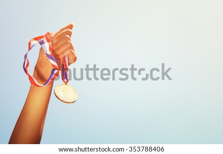 woman hand raised, holding gold medal against sky. award and victory concept
