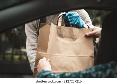 Woman Hand Receiving Shopping Brow Paper Bag Out Of Car Open Window Driving Thru Pickup From Seller With Blue Glove - View From The Car Inside - Room For Text Or Copyspace