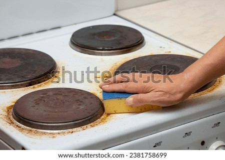 Woman hand remaining burnt stains on dirty white electric stove scrubbing using sponge