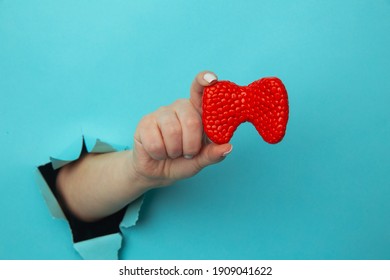Woman hand showing a thyroid out of a hole torn in blue paper wall. Health care, pharmaceutics and medicine advertisement