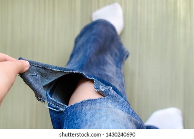 Woman hand shows a hole on a jeans. Woman dressed in a blue jeans with a large hole below the knee on a left pant leg. Holey jeans. Top down view.