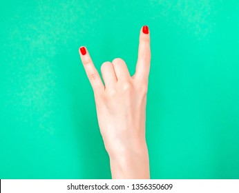 Woman hand shows Rock N Roll Hand Signs isolated on turquoise green color background. Sign of the horns. If you re feeling super cool, do the rock n roll hand sign
