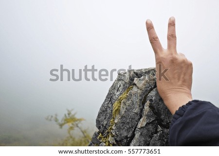 A woman hand shows victory sign above the rough stone after climbing to the top of the mountain. Victor, winner and successful concept. Conquering the problem concept.