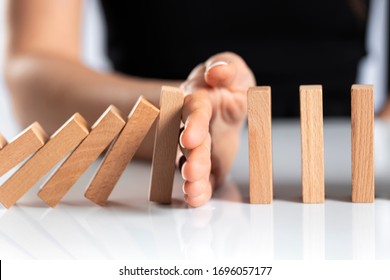 Woman hand stopping falling wooden dominoes effect on white solid ground