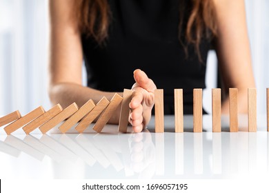 Woman hand stopping falling wooden dominoes effect on white solid ground