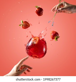 Woman hand support fly glass of strawberry drink with splash, juice strawberries falling in glass. Cocktail of strawberry and lavender flavor. Summer art food concept on pink background