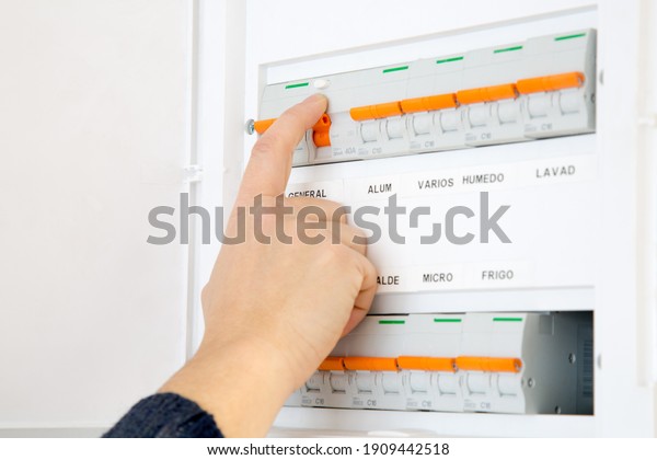 Woman hand switching off the fuse box at home.\
Words in spanish