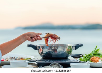 Woman Hand Take River Prawn And Put It In Boiling Pot Shabu Shabu Hotpot Style In Japanese Restaurant. Shabu Shabu Dinner Near Swimming Pool. Sukiyaki Dish Of Pork, Shrimp, Seafood, Fresh Vegetables.