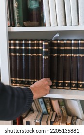 Woman Hand Takes A Religious Jewish Book From A Bookcase Shelf. Jewish Religious Education