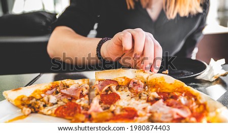 woman Hand takes a slice of meat Pizza with Mozzarella cheese, salami, Tomatoes, pepper, ham, Spices and chicken in cafe