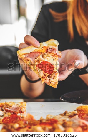 woman Hand takes a slice of meat Pizza with Mozzarella cheese, salami, Tomatoes, pepper, ham, Spices and chicken in cafe