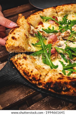 woman Hand takes a slice of meat Pizza with Mozzarella cheese, ham, bacon, Spices and chicken in cafe outdoor