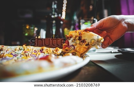 woman Hand takes a slice of meat Pizza with Mozzarella cheese, salami, Tomatoes, pepper, ham in cafe