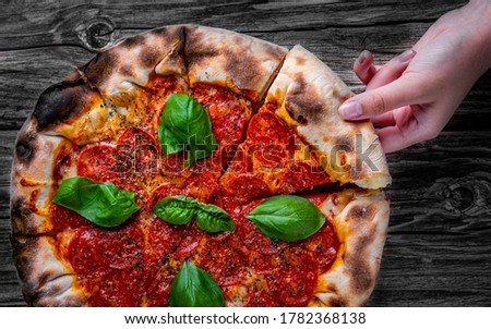 woman Hand takes a slice of Pepperoni Pizza with Mozzarella cheese, salami, Tomatoes, pepper, Spices and Fresh Basil. Italian pizza on wooden table background