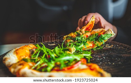 woman Hand takes a slice of Pepperoni Pizza with Mozzarella cheese, salami, Tomatoes, pepper, Spices and Fresh arugula