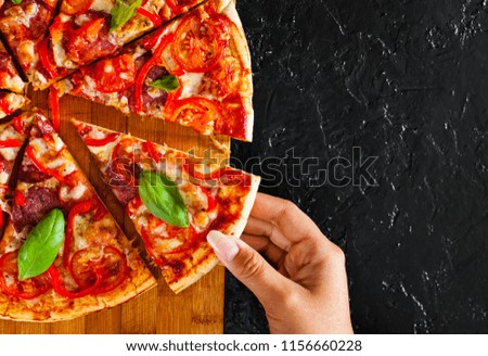 woman Hand takes a slice of Pizza with Mozzarella cheese, Ham, Tomatoes, salami, pepper, pepperoni, Spices and Fresh Basil. Italian pizza on black background. with copy space. top view