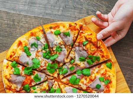 woman Hand takes a slice of Pizza with Mozzarella cheese, ham, pepper, meat, Tomato sauce, Spices and Fresh Basil. Italian pizza on wooden background