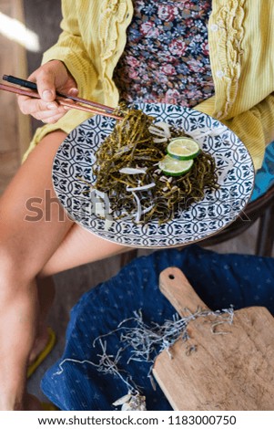 Woman hand takes and twirls with chopsticks a chuka laminaria seaweed salad with lime, lemon juice, garlic, onion on plate. Traditional Japanese, Chinese, Korean asian seafood. Healthy vegan lunch