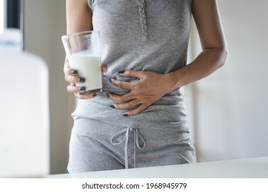 Woman hand touch stomach as stomachache and pain holding a glass of milk as dairy intolerant lactose intolerance allergy health care concept