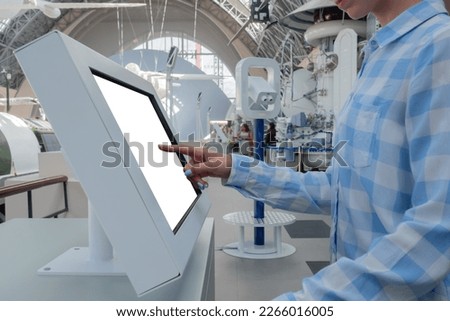 Woman hand touching blank interactive touchscreen white display of electronic kiosk at futuristic exhibition or museum: close up. White screen, mock up, copyspace, template, technology concept.