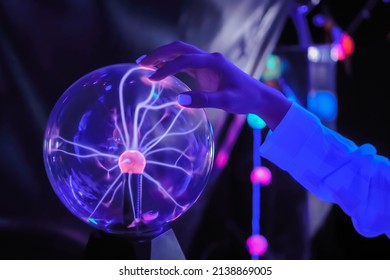 Woman hand touching plasma ball with many energy rays inside in dark room - close up view. Electricity, education, science, futuristic and physics concept