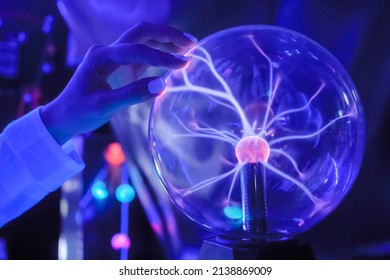 Woman hand touching plasma ball with many energy rays inside in dark room - close up view. Electricity, education, science, sci-fi, futuristic and physics concept