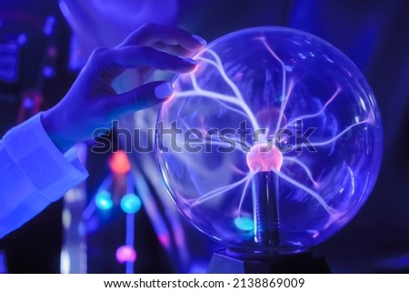 Woman hand touching plasma ball with many energy rays inside in dark room - close up view. Electricity, education, science, sci-fi, futuristic and physics concept