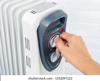 Woman Hand Turns On The Thermostat Knob Of An Electric Oil Heater. White Oil-filled Radiator For Home And Office. House Heating And Comfort. Front View.