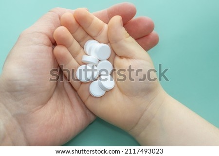 woman hand under a kid's hand, that is holding a stack of white round tablets. medicine concept. treatment. green smooth background. vitamins, calcium, probiotics, virus. healthcare