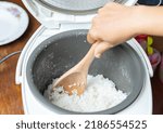 Woman hand use wooden ladle scoop rice in the electric rice cooker.