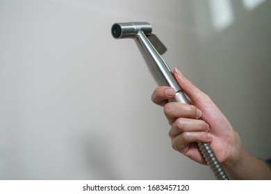 Woman hand using Chromium bidet shower sitting on toilet.
