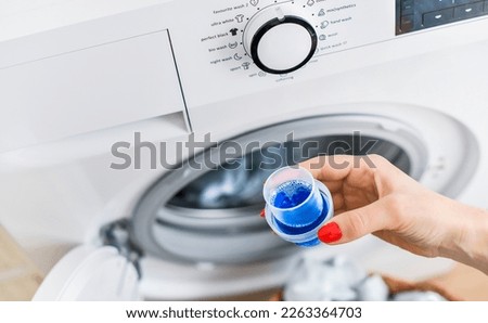 Woman hand using or filling detergent in the washing machine. Pour blue washing liquid, wash machine blured in background.