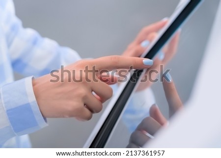 Woman hand using interactive touchscreen display of white electronic multimedia kiosk at technology exhibition - scroll and touch - close up. Education, learning, entertainment concept