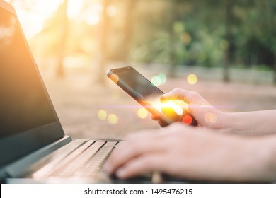 Woman Hand Using Smart Phone And Laptop At Outdoor Nature Park And Sunset Sky With Bokeh Light Abstract Background. Technology Business And Freelance Working Concept. Vintage Tone Filter Effect Color 