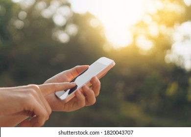 Woman Hand Using Smart Phone At Outdoor Nature Park With Sunset Sky Abstract Background. Copy Space Technology Business And Travel Nature Holiday Concept. Vintage Tone Filter Effect Color Style.