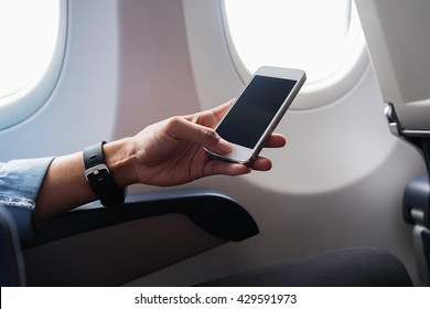 Woman Hand Using Smart Phone On Airplane. Female Traveler Using Smart Phone In Passenger Cabin. Can Be Add Your Texts Or Others On Screen. Sun Shining Trough Airplane Window. Technology Concept.
