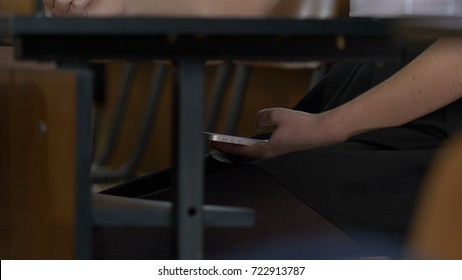 Woman Hand Using A Smart Phone Under A Wooden Table. Woman Uses The Internet On Your Phone During The Exam