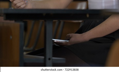 Woman Hand Using A Smart Phone Under A Wooden Table. Woman Uses The Internet On Your Phone During The Exam