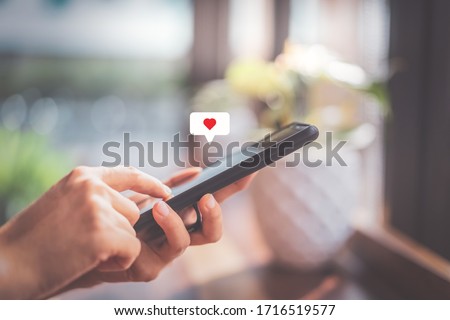 Woman hand using smartphone with heart icon at coffee shop background. Technology business and social lifestyle concept. Vintage tone filter effect color style.